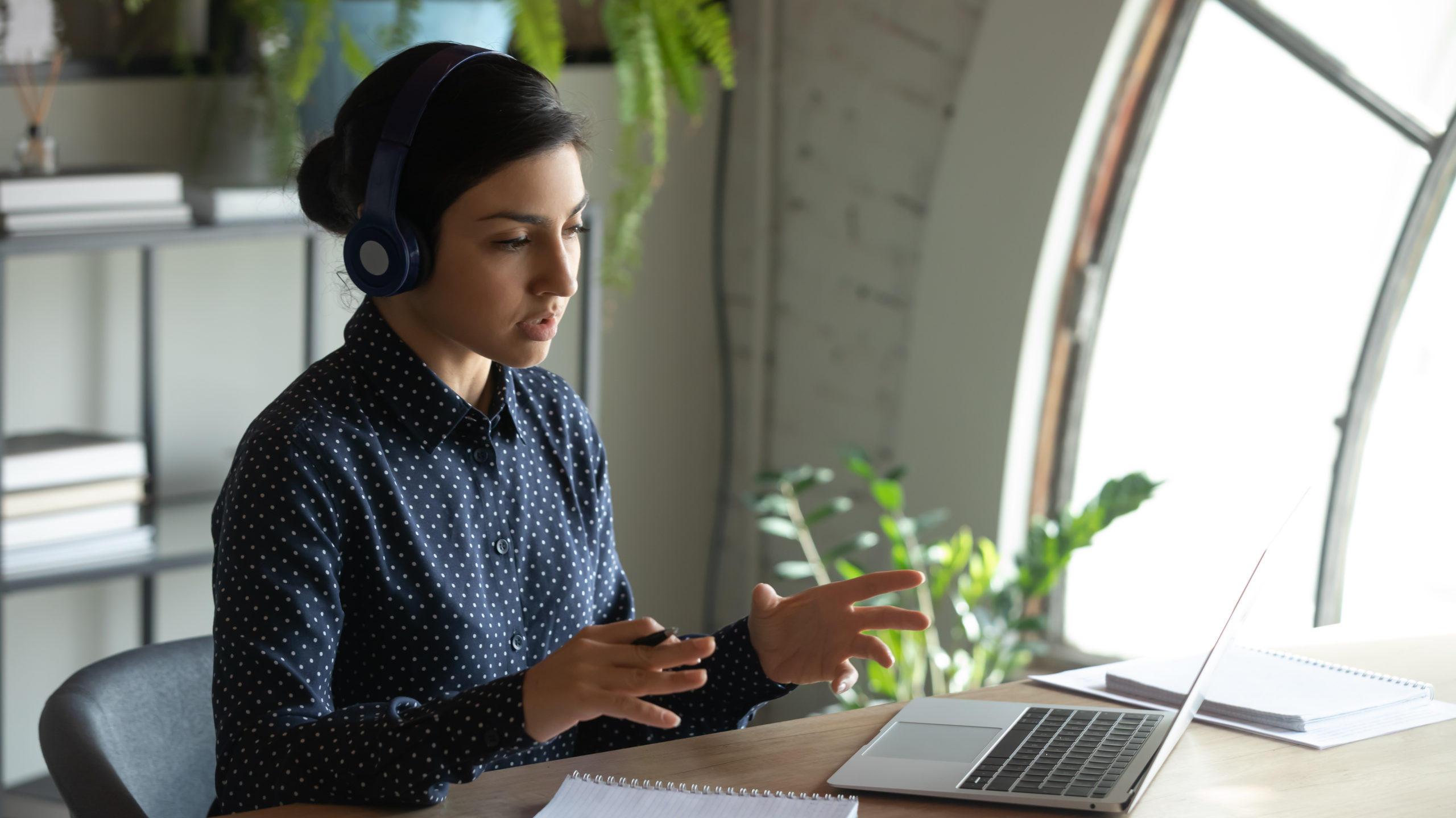 A young multiracial woman wearing a video conference headset and speaking on a conference call