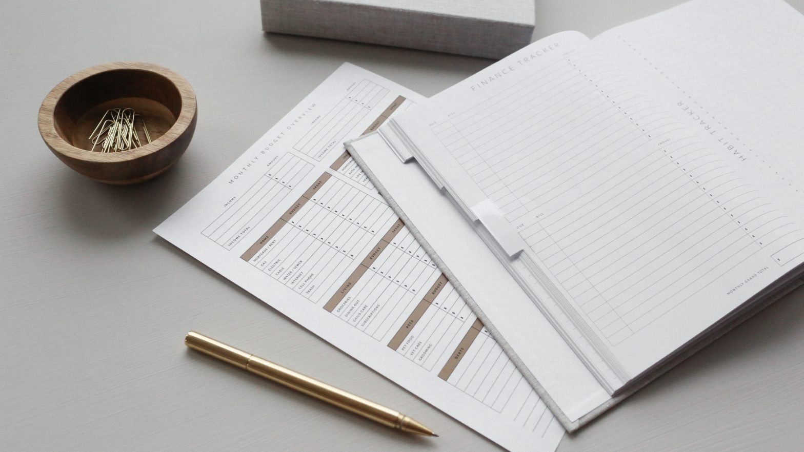 A photo of budgeting and financial documents on a grey desk with a pencil and gold paperclips