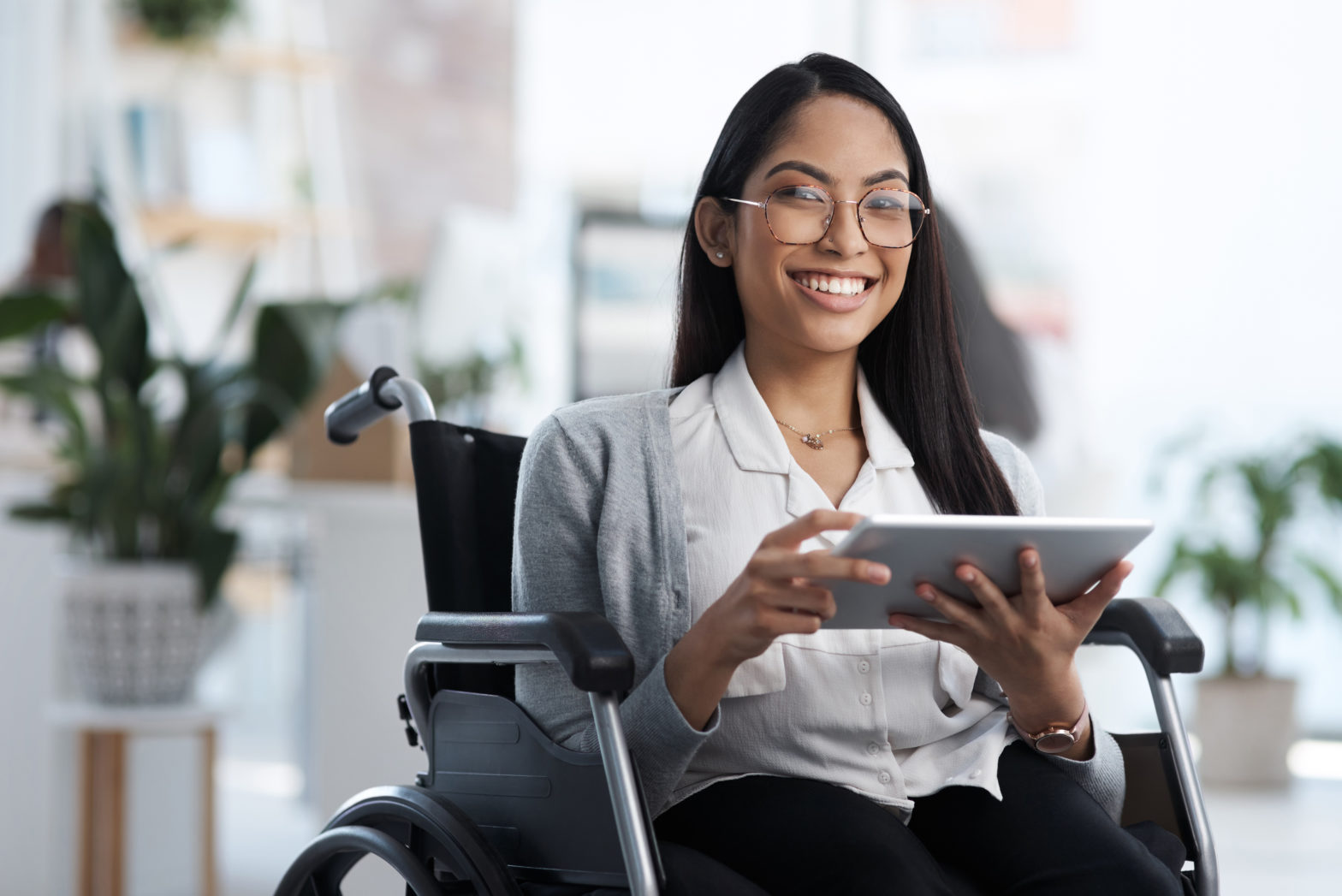 A photo of a smiling young woman holding an ipad and using a wheelchair
