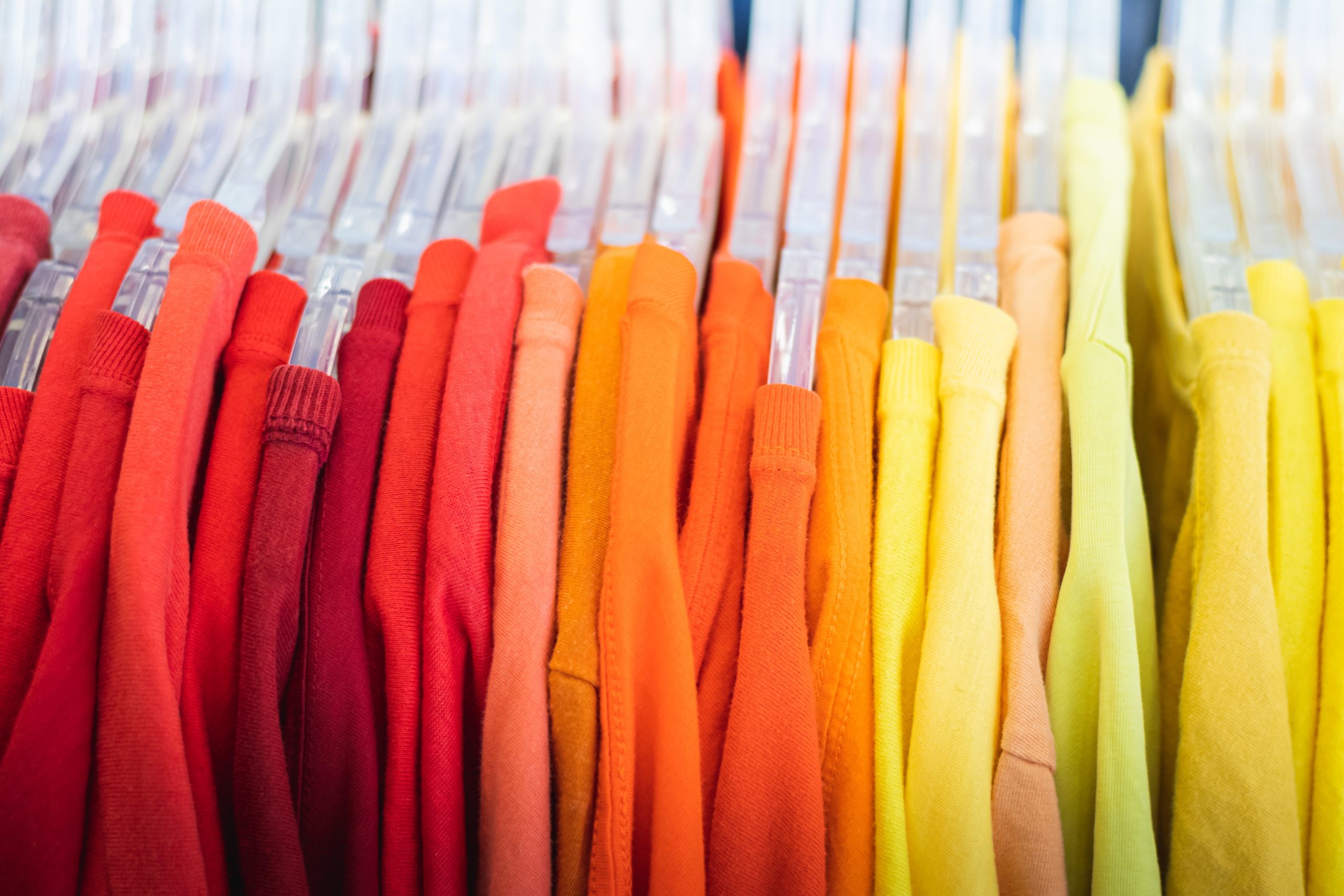 Brightly coloured sweaters hanging on a rack in order of red on the left, orange in the middle, and yellow on the right