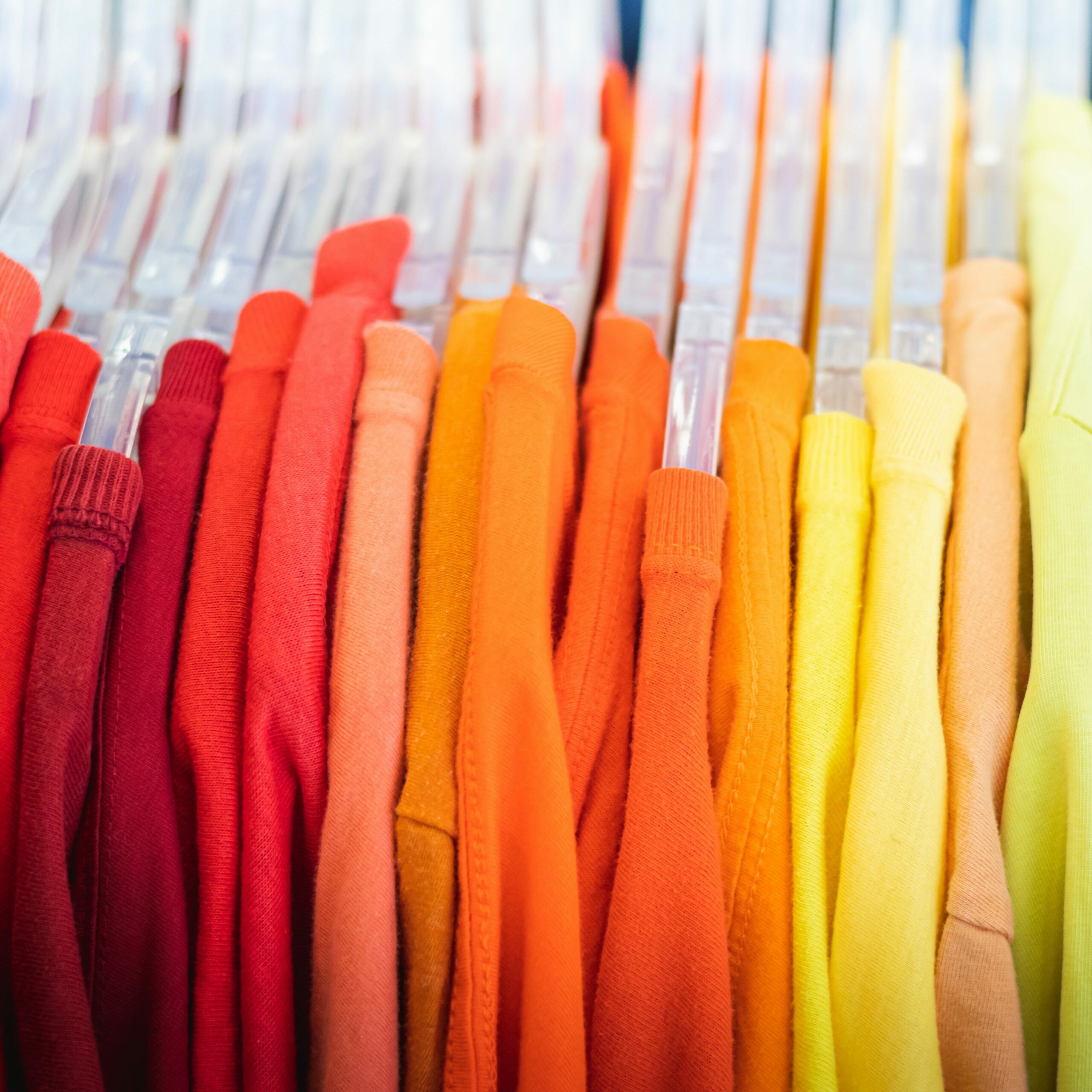 Brightly coloured clothes hanging on a rack in order of red on the left, orange in the middle, and yellow on the right