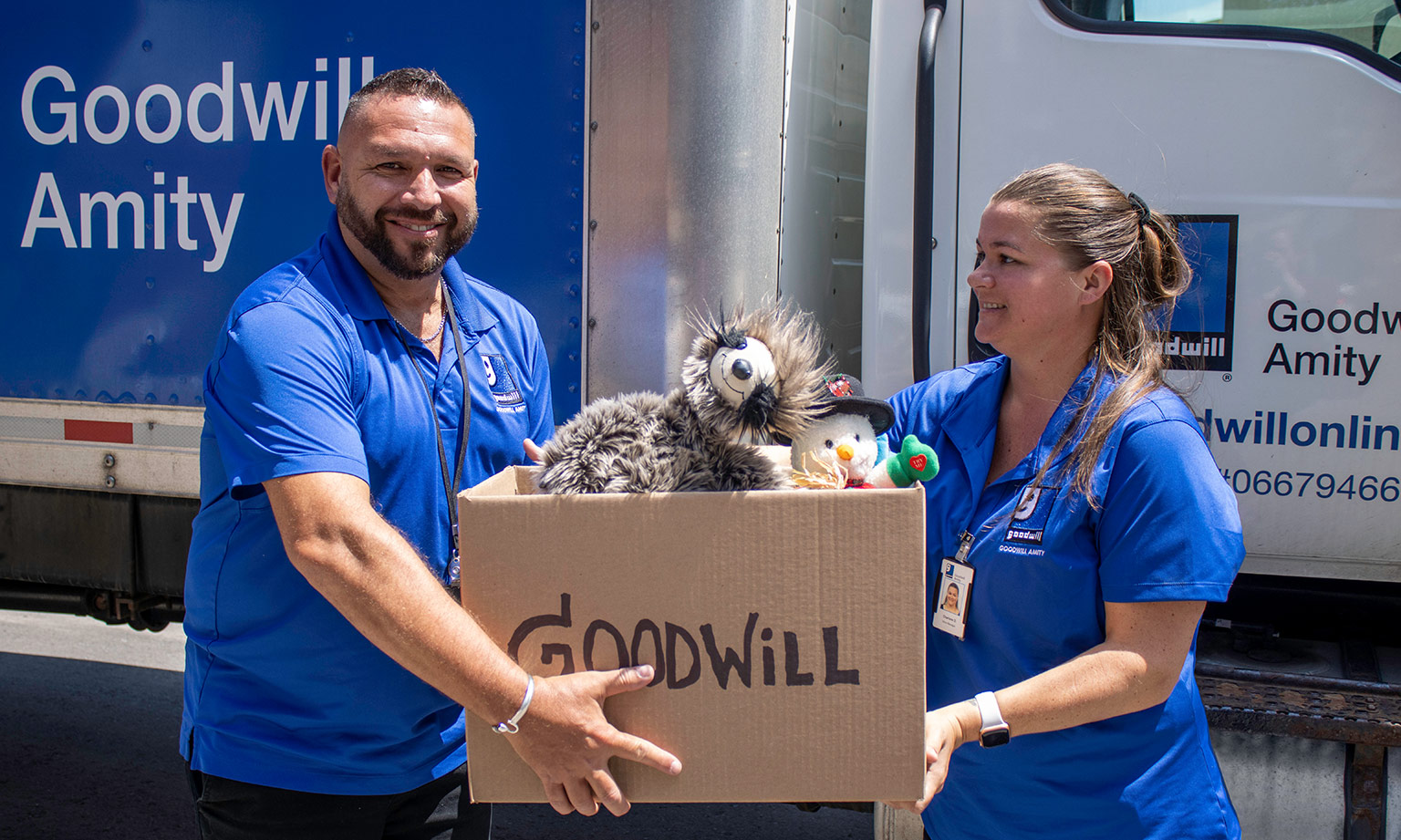 Two Goodwill employees holding a donation box in front of the donation truck